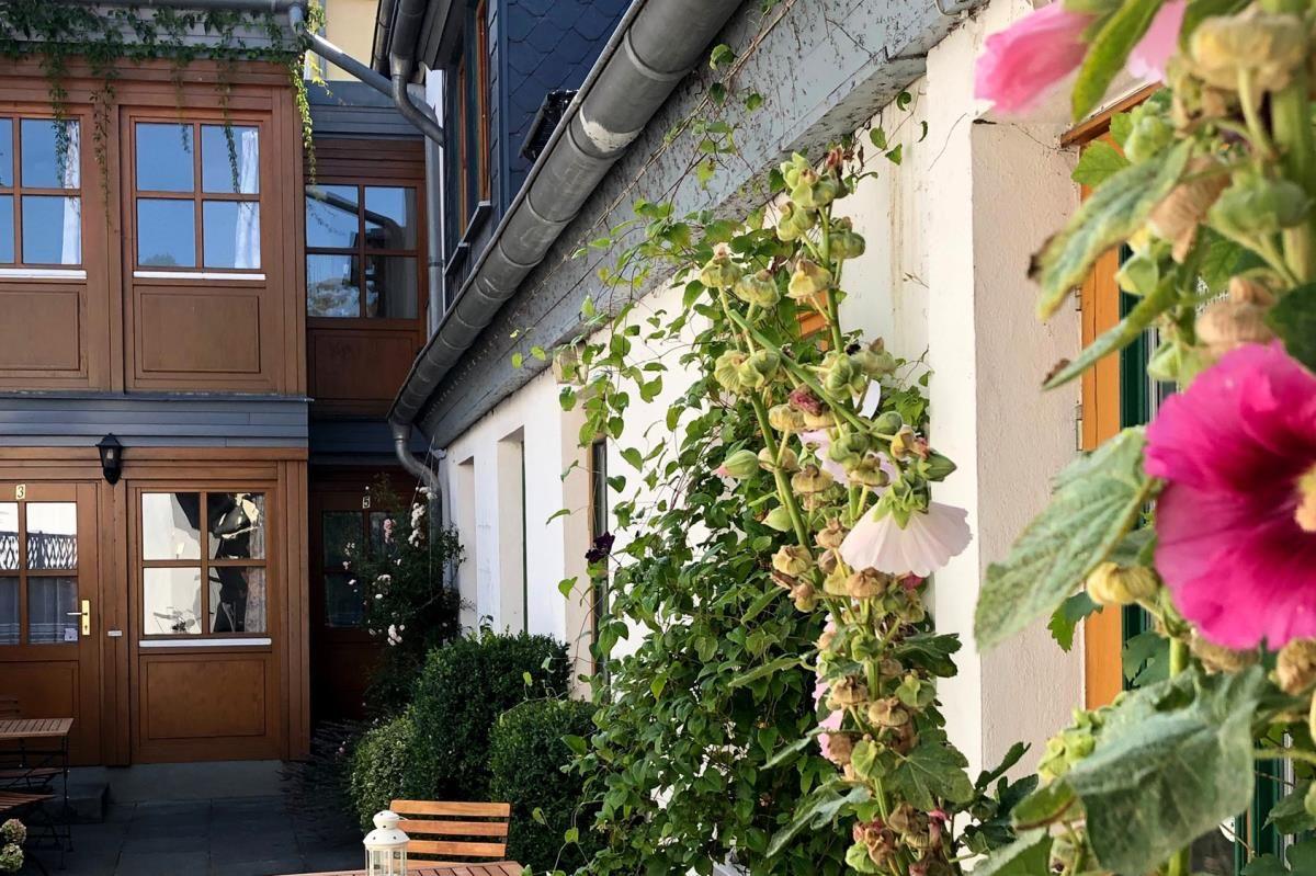 Weiße Villa mit grünen Fensterrahmen und Dachterrasse an einer gepflasterten Straße.