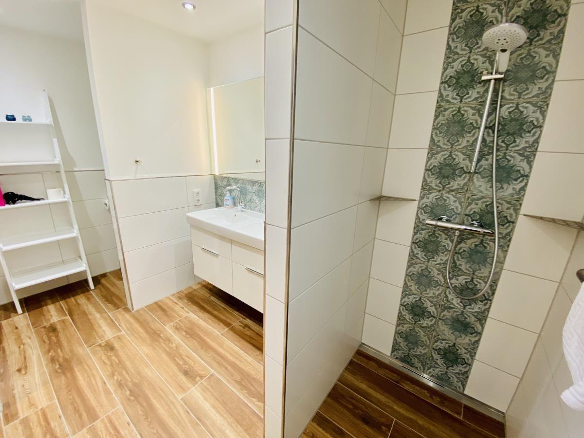 Badezimmer mit Waschbecken, Spiegel, Toilette und Holzoptik-Bodenfliesen.