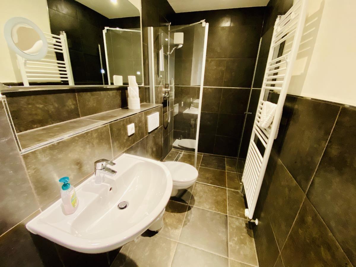 Badezimmer mit Dusche, Waschbecken und Toilette. Fliesenwand und Boden.