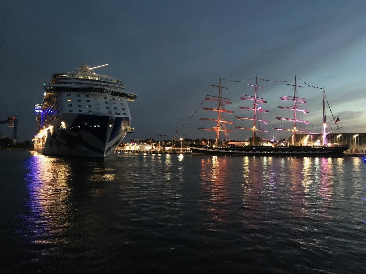 Großes Kreuzfahrtschiff liegt am Hafen mit klarer Wasseroberfläche und blauem Himmel.