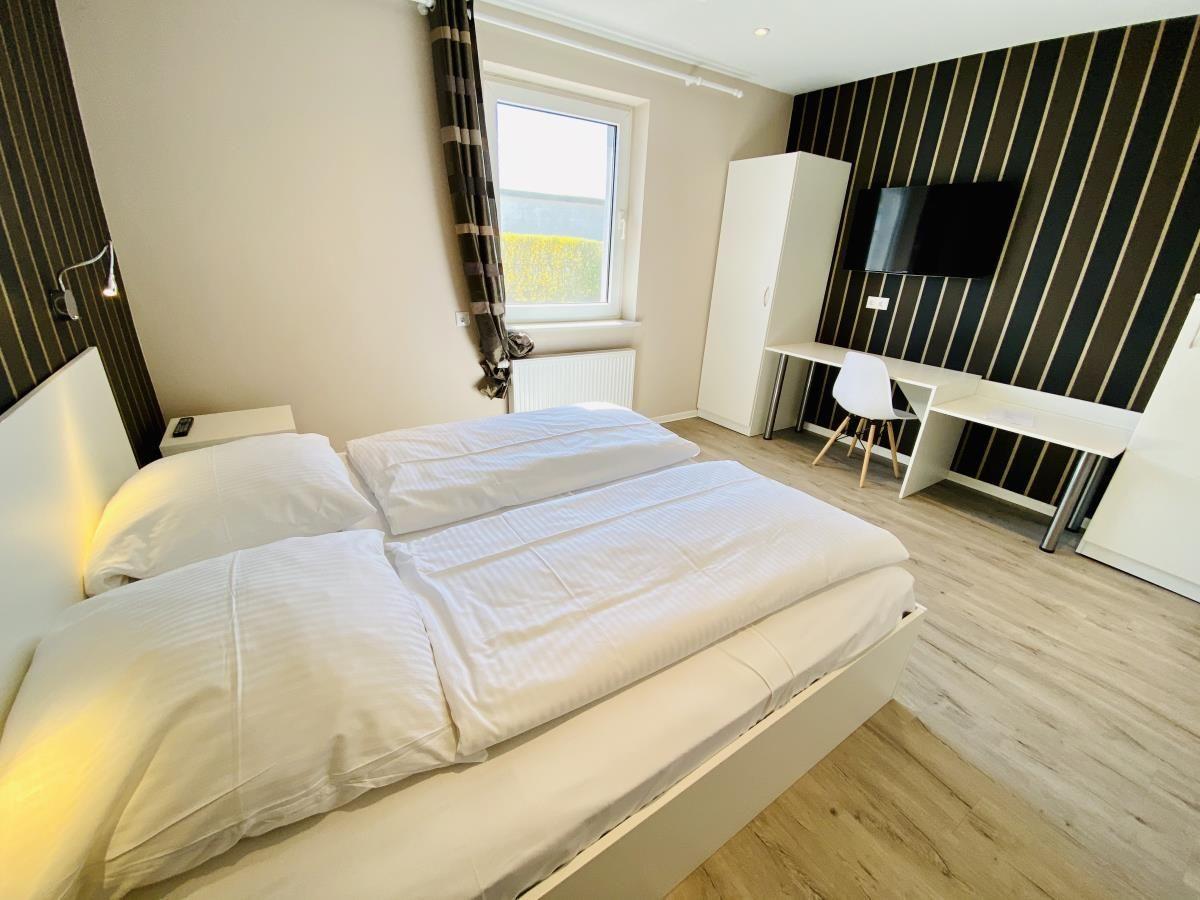 Zimmer mit zwei Betten, gestreifter Wand und Holzboden.