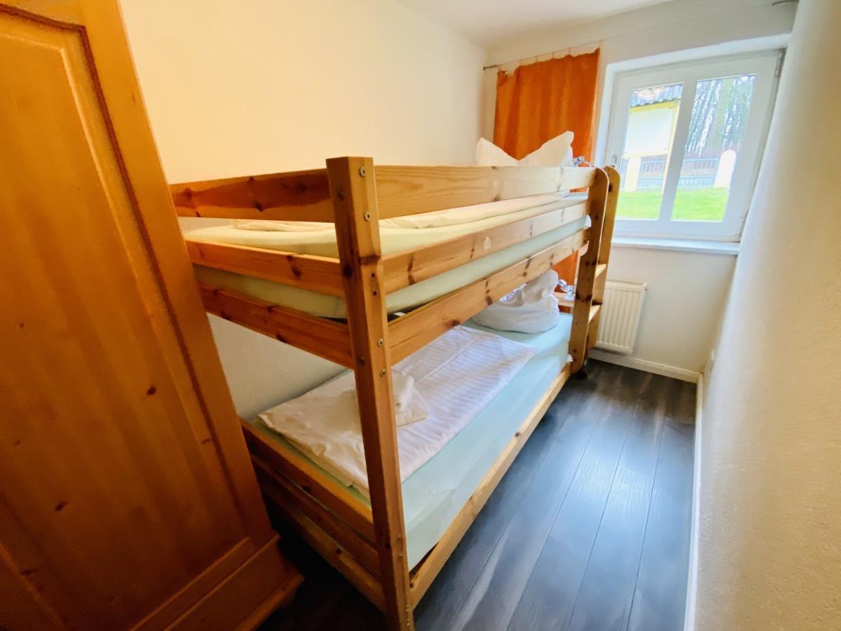 Zimmer mit Holz-Etagenbett, Kleiderschrank und Tür zum Flur.