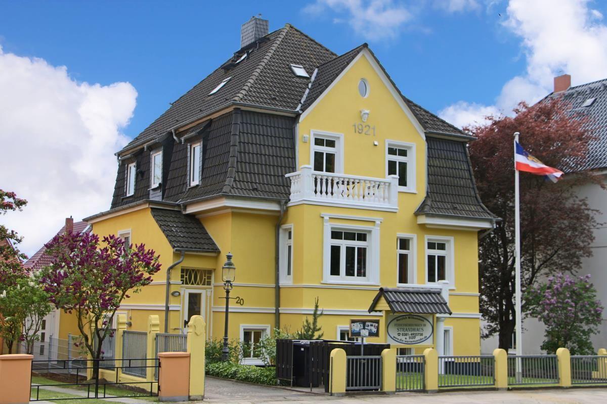 Gelbes Haus mit Balkonen und gepflastertem Hof. Silberner Wagen parkt vorne.