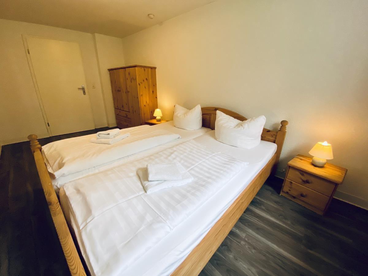 Ein Schlafzimmer mit Holzbett, Schrank und Fenster mit Vorhang.