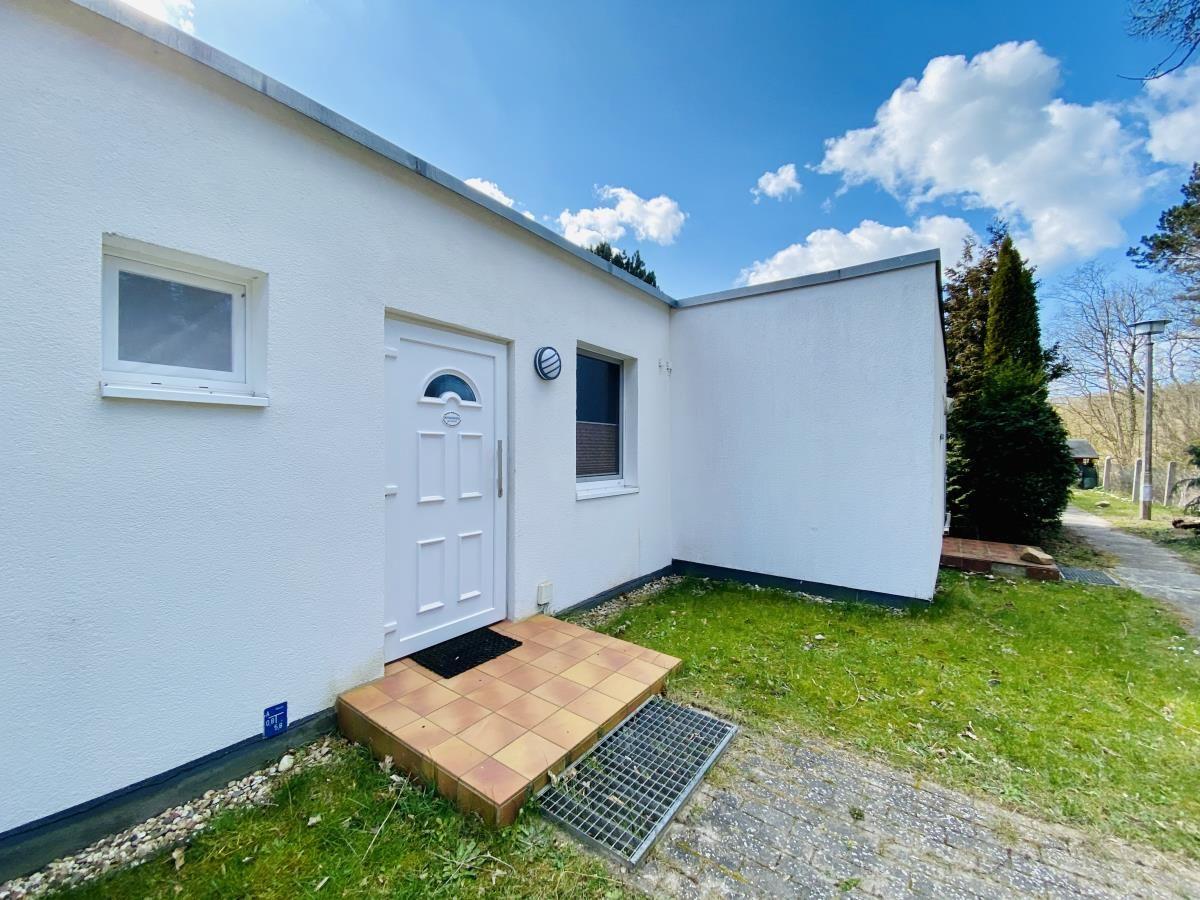 Haus mit Terrasse, rotem Sonnenschirm und Garten. Holzschuppen und Pflanzen sind sichtbar.