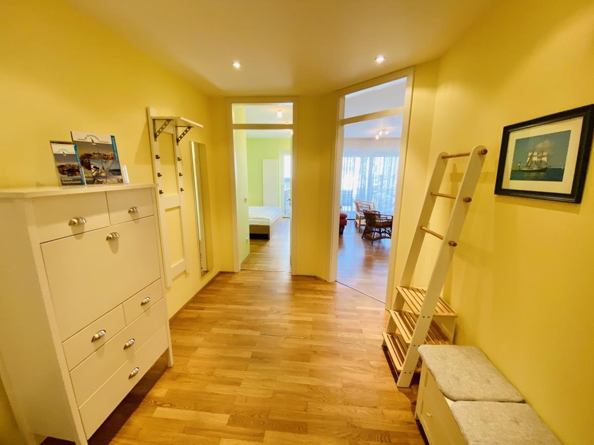 Flur mit Holzboden, Kleiderständer und Schuhschrank. Türen und Wandfarbe sind weiß.