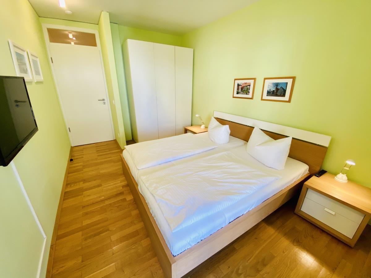 Schlafzimmer mit Doppelbett, Holzboden und Balkontür.