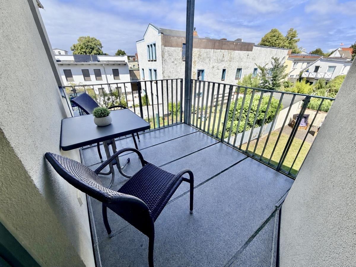 Villa mit Balkon und grüner Hecke vor einem klaren Himmel.