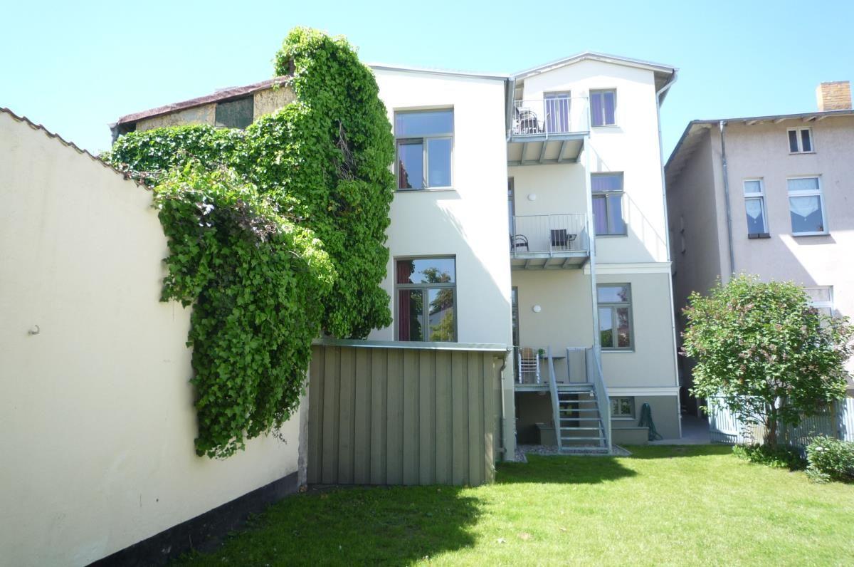 Hinterhof mit zwei Holzliegestühlen, Rasenfläche und weißem Zaun.