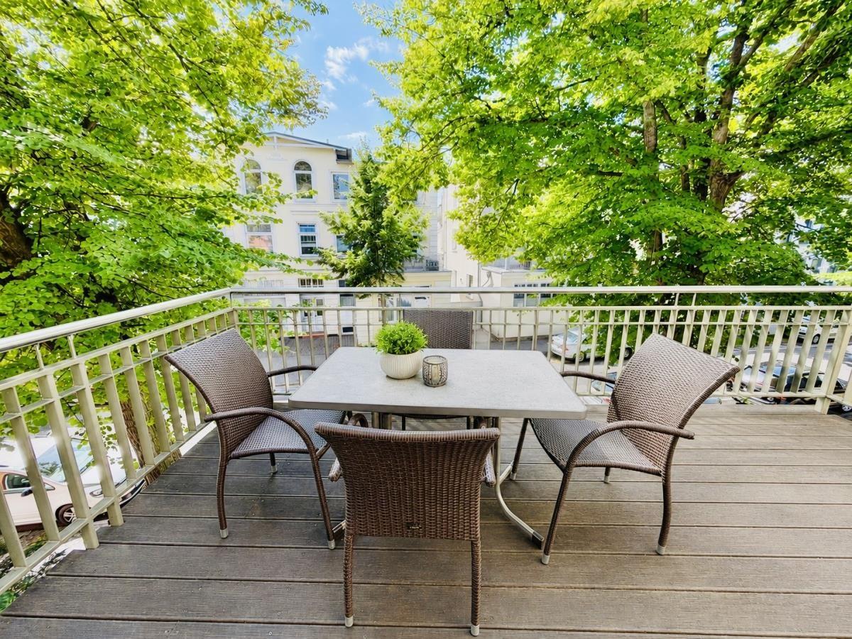 Ein mehrstöckiges Haus mit Balkon und Fenstern, umgeben von Bäumen und geparkten Autos.