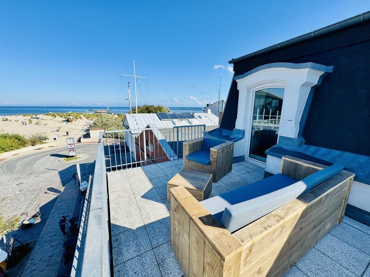 Terrasse mit Blick auf Leuchtturm und Strand. Holzmöbel und Metallgeländer.