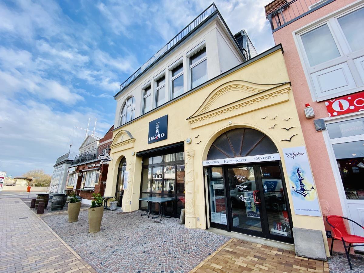 Wohnzimmer mit Sofa, Tisch, Stühlen und Fenster. Wanduhr und Fernseher angebracht.