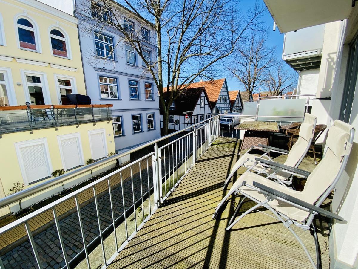 Weißes Mehrfamilienhaus mit Balkonen und Garage an einer Straße mit Bäumen.