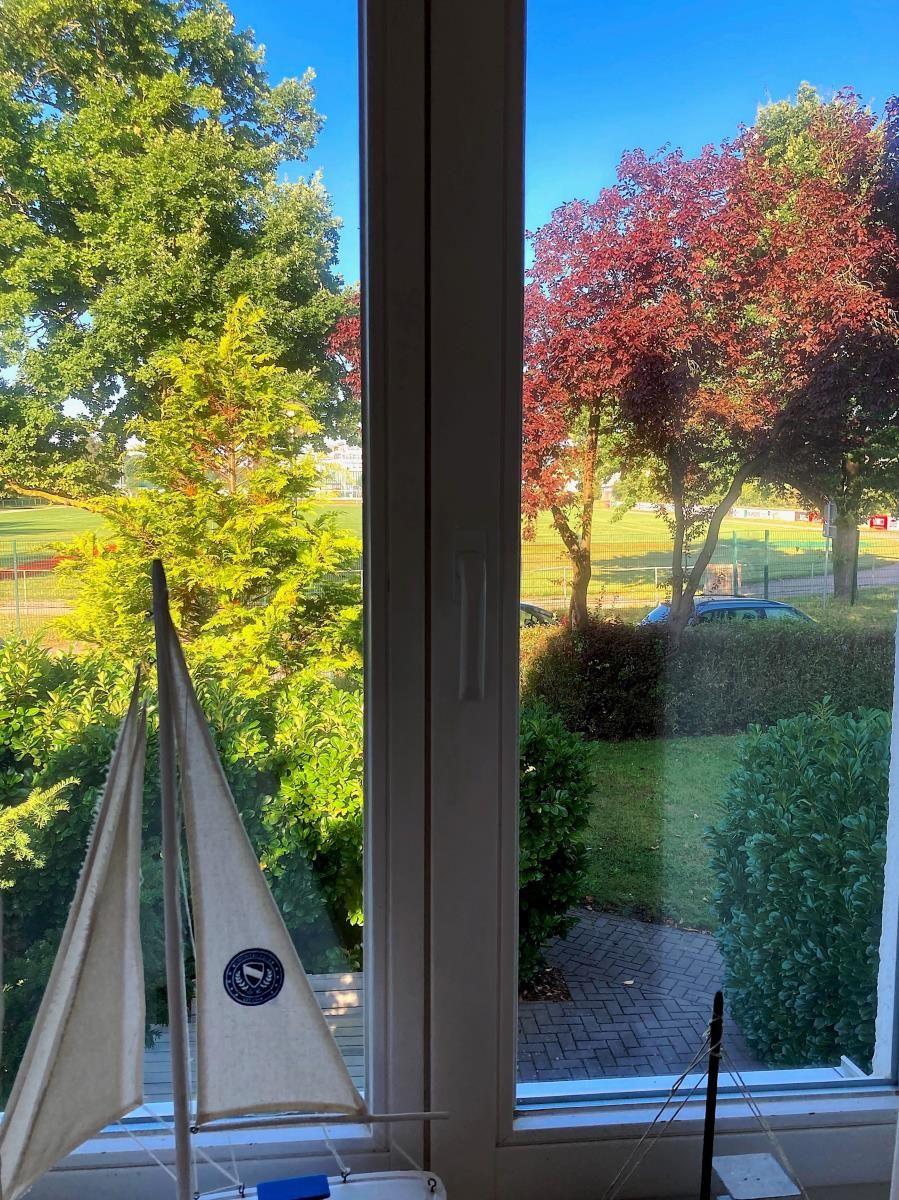 Durch die Glastüren blickt man auf einen Balkon mit Blick auf einen grünen Garten.