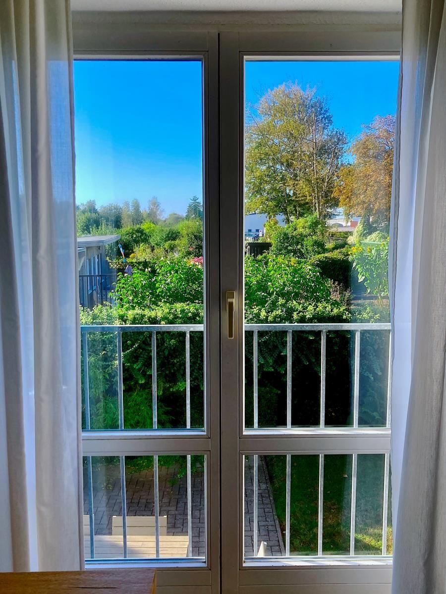 Zimmer mit Fenster, blauen Vorhängen, Tischlampe und Segelschiffmodell.
