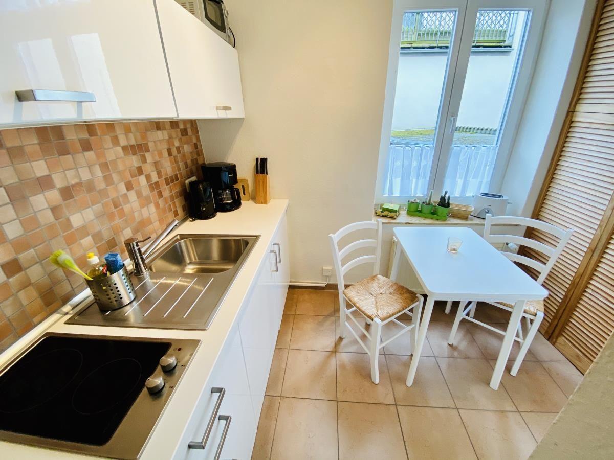 Küche mit weißem Tisch und Stühlen, Fenster mit Vorhängen und Küchenzeile mit Spüle.