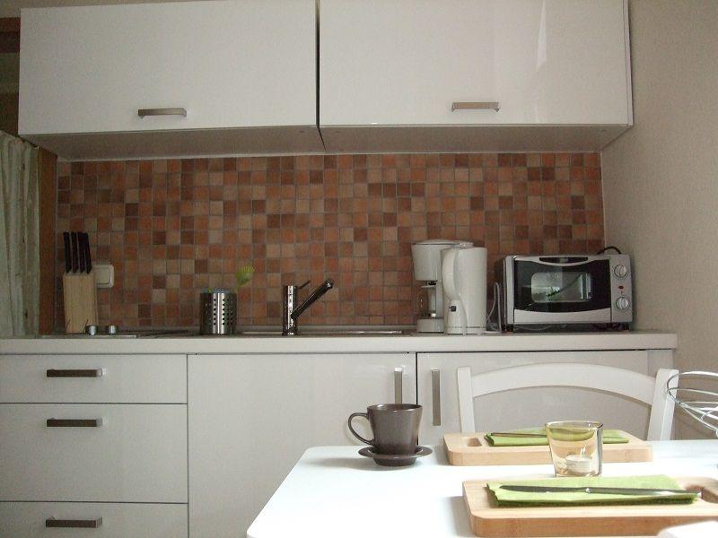 Küche mit Essbereich, Fenster und Holzschrank. Tisch mit Stühlen und Küchengeräten.