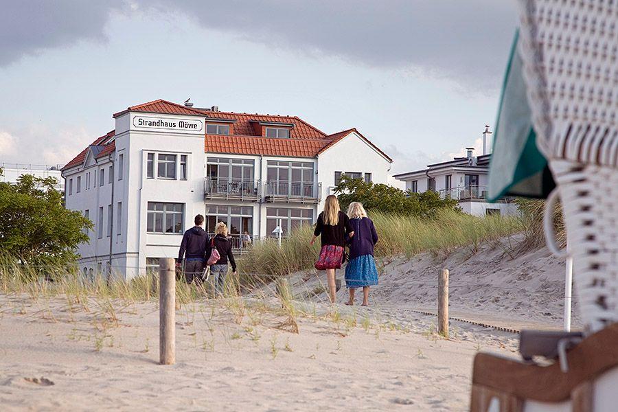 Strandhaus Möwe mit Balkonen und rotem Dach, umgeben von Bäumen und Gras.