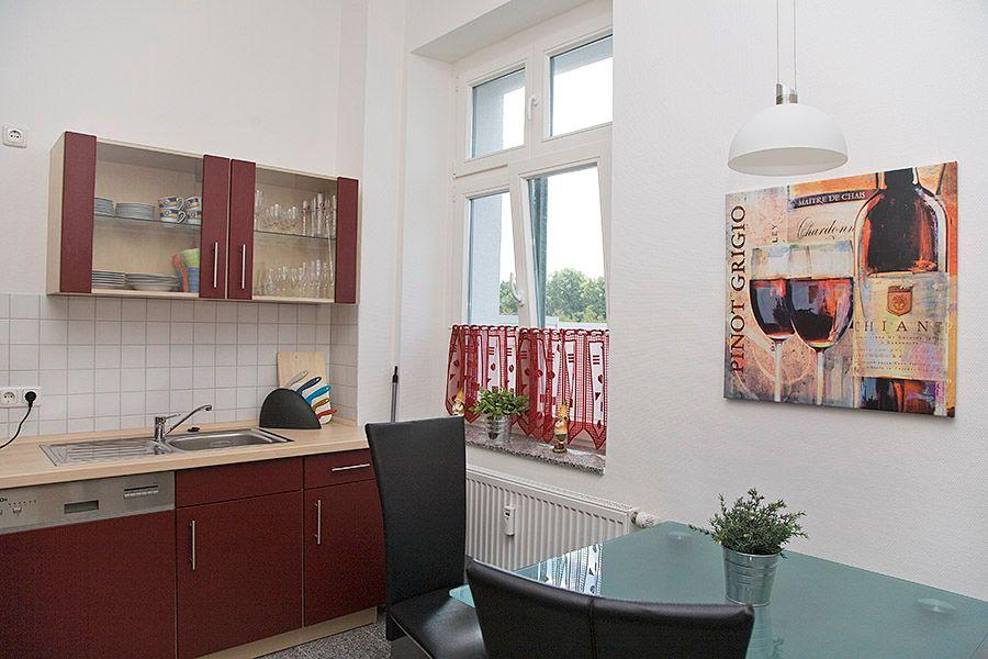 Küche mit roten Schränken und Essbereich mit Glasplatte.