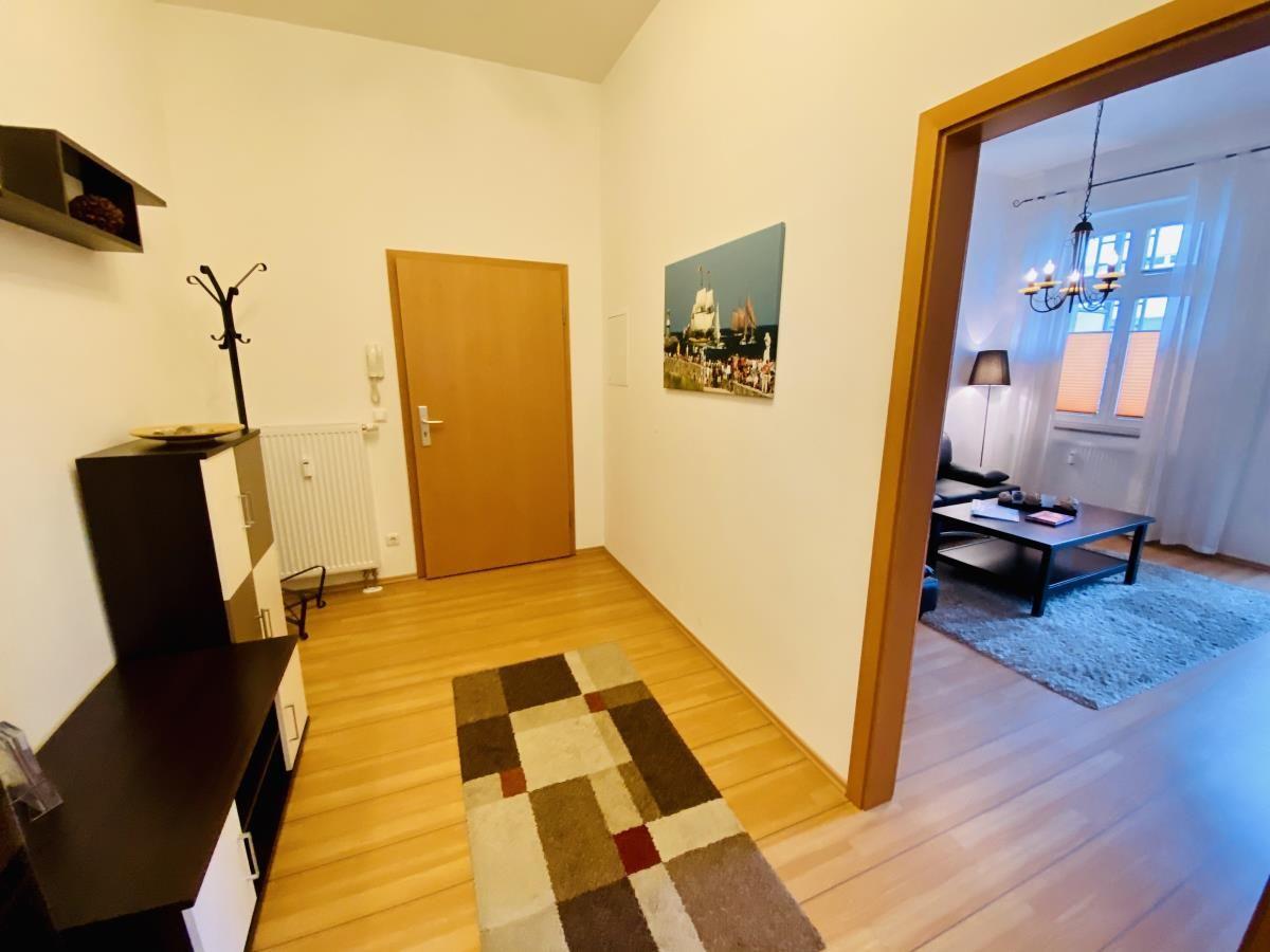 Flur mit Holzboden, Kleiderständer und Schrank. Teppich und Wandspiegel sichtbar.