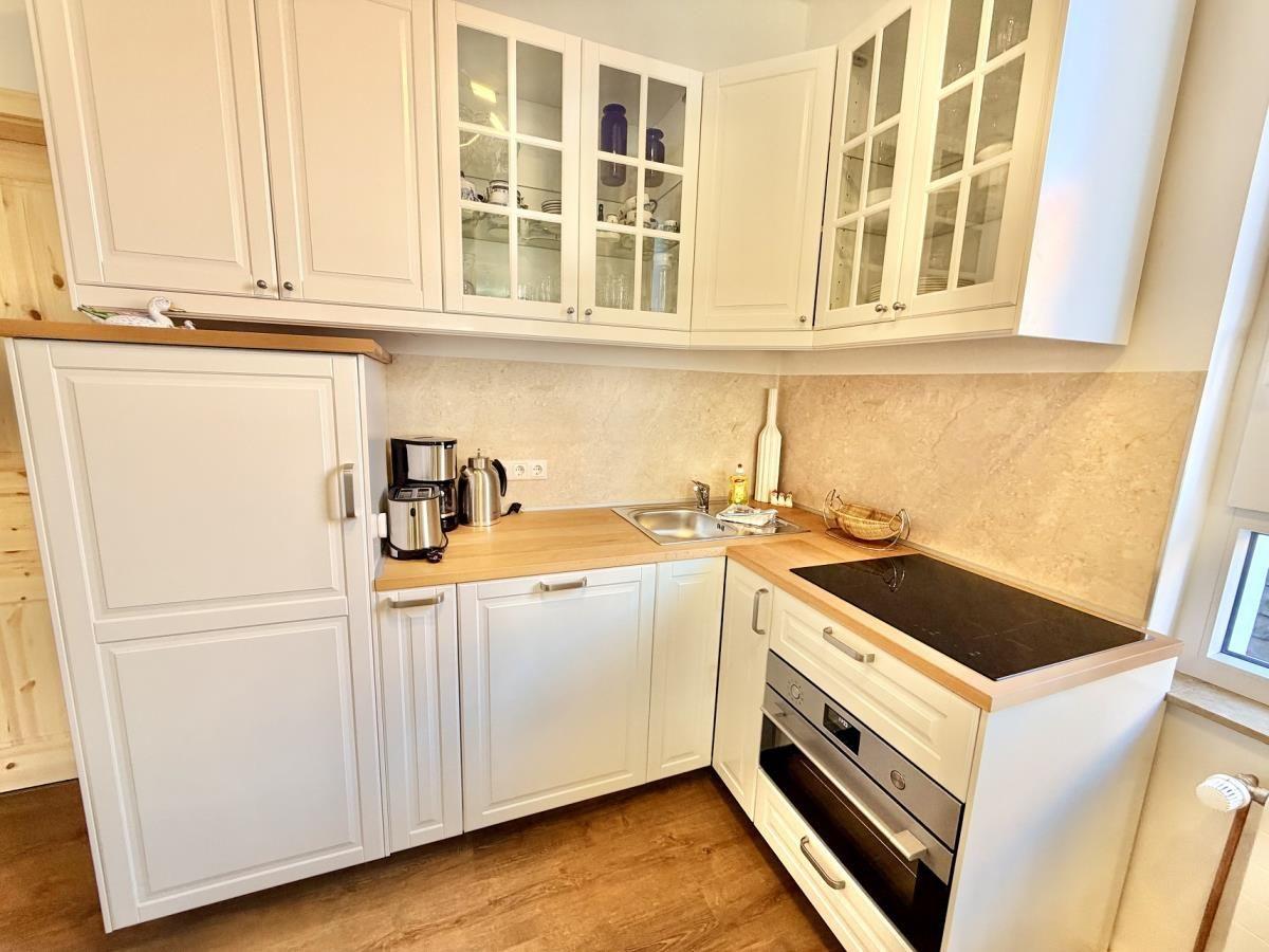 Essbereich mit Holztisch und Stühlen. Küche mit weißen Schränken im Hintergrund.