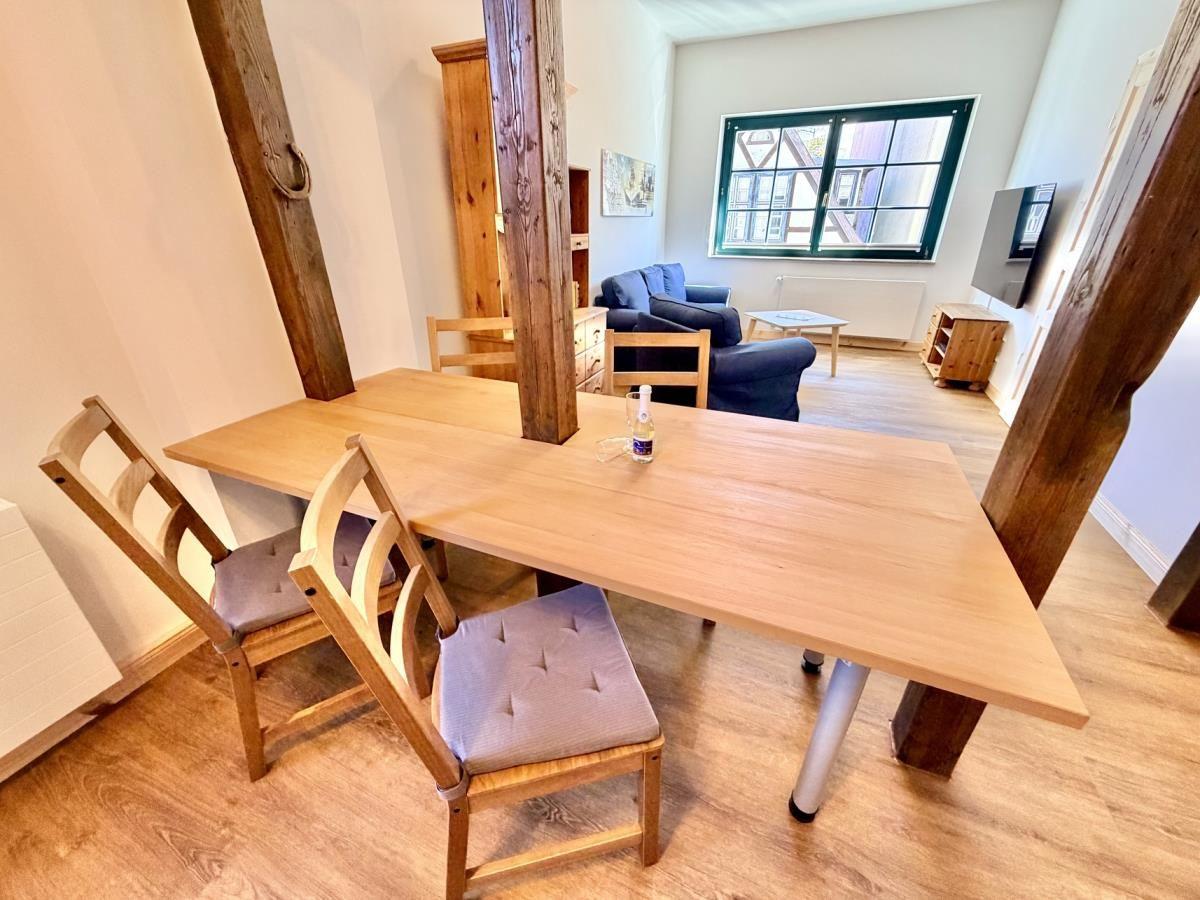 Schlafzimmer mit Holzbett und Tisch. Im Hintergrund Wohnzimmer mit Sofa und Essbereich.