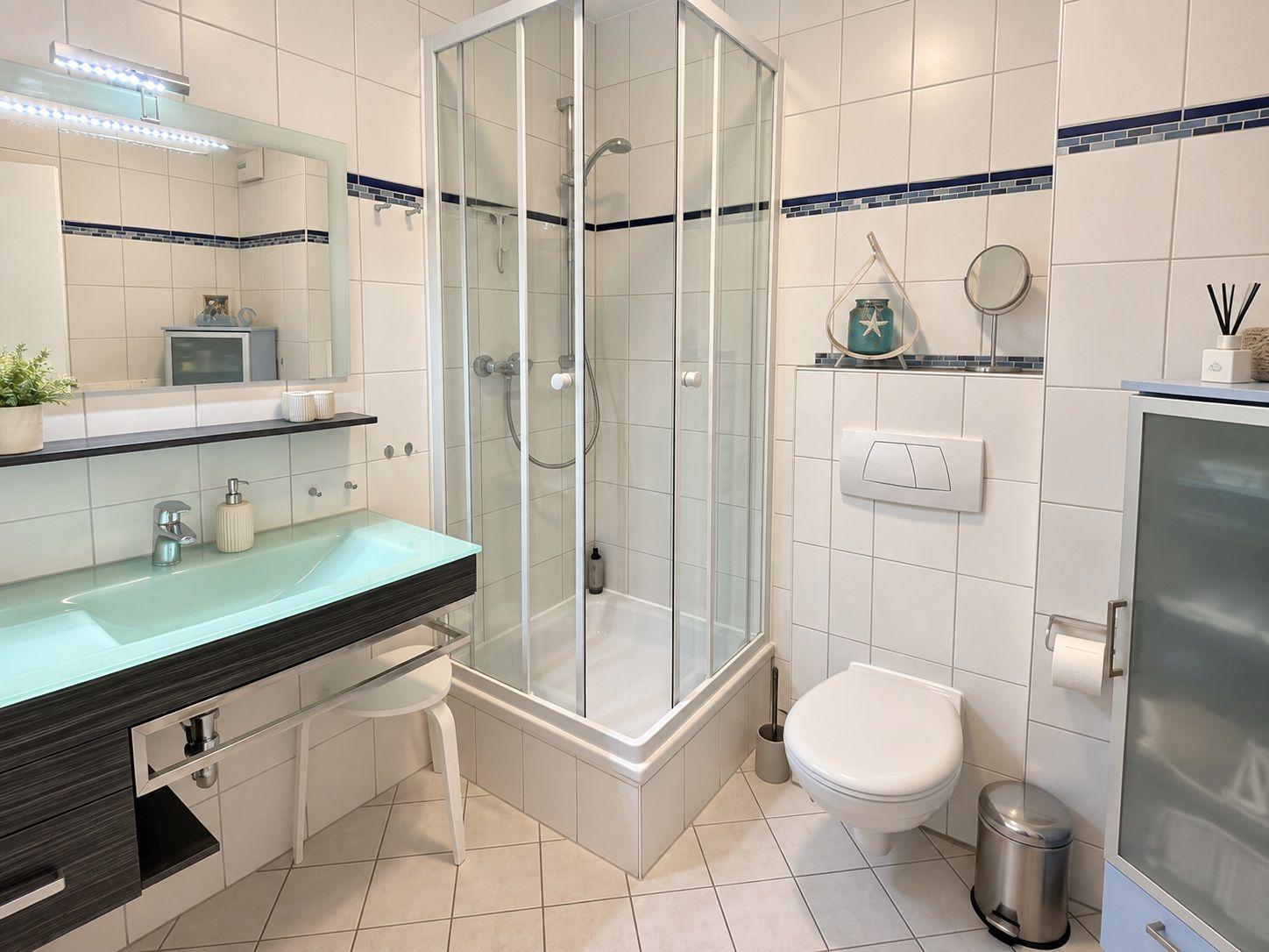 Badezimmer mit Dusche, Waschbecken und WC. Fliesenwand und Boden.
