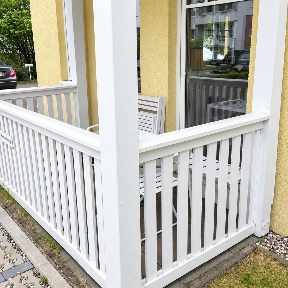 Weiße Veranda mit Geländer und Stühlen vor gelbem Haus