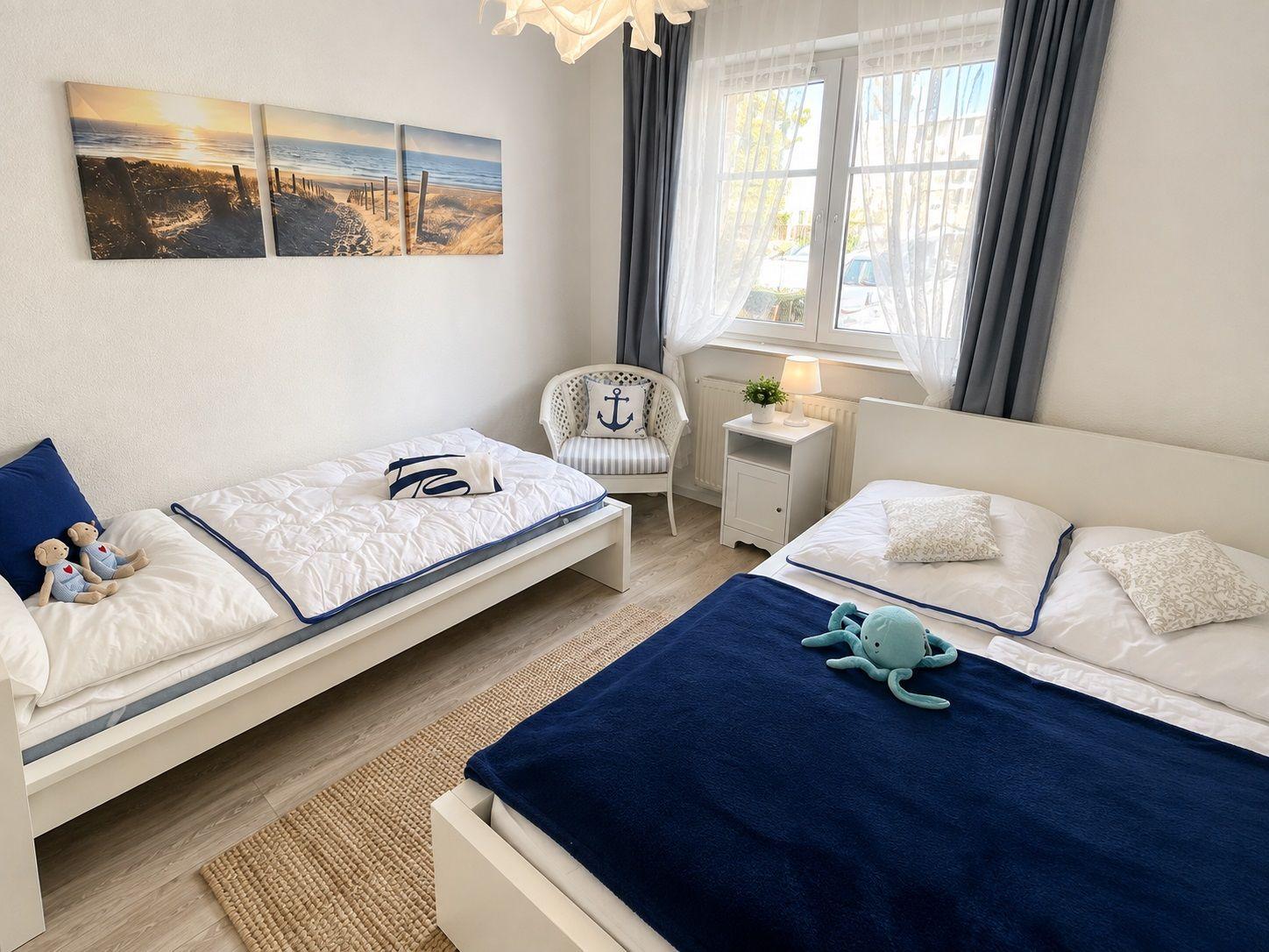 Zimmer mit zwei Betten, Fenster, Stuhl und Wandbildern.