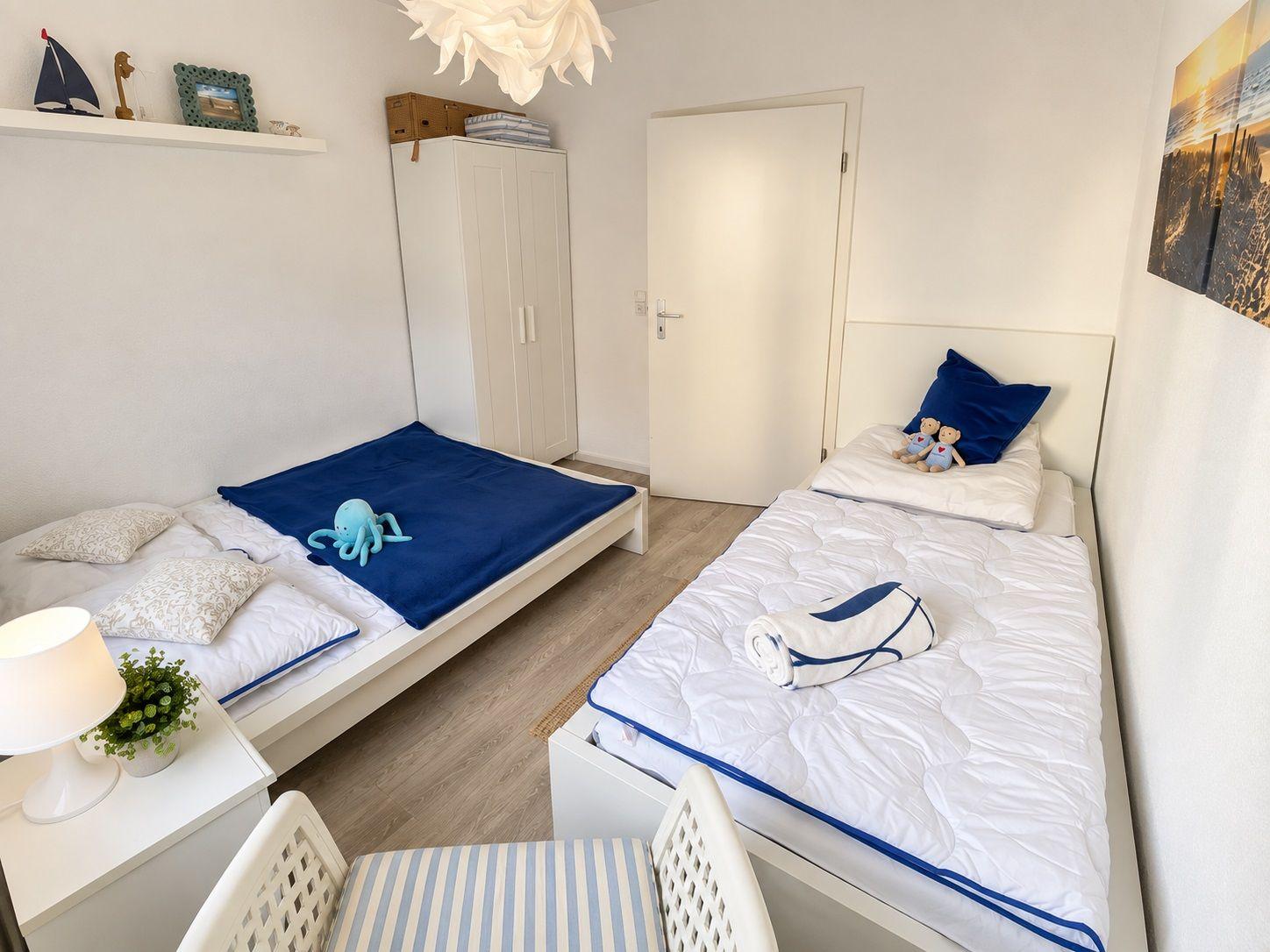 Zwei Betten mit blauen Decken, Kleiderschrank und Tür im Schlafzimmer.