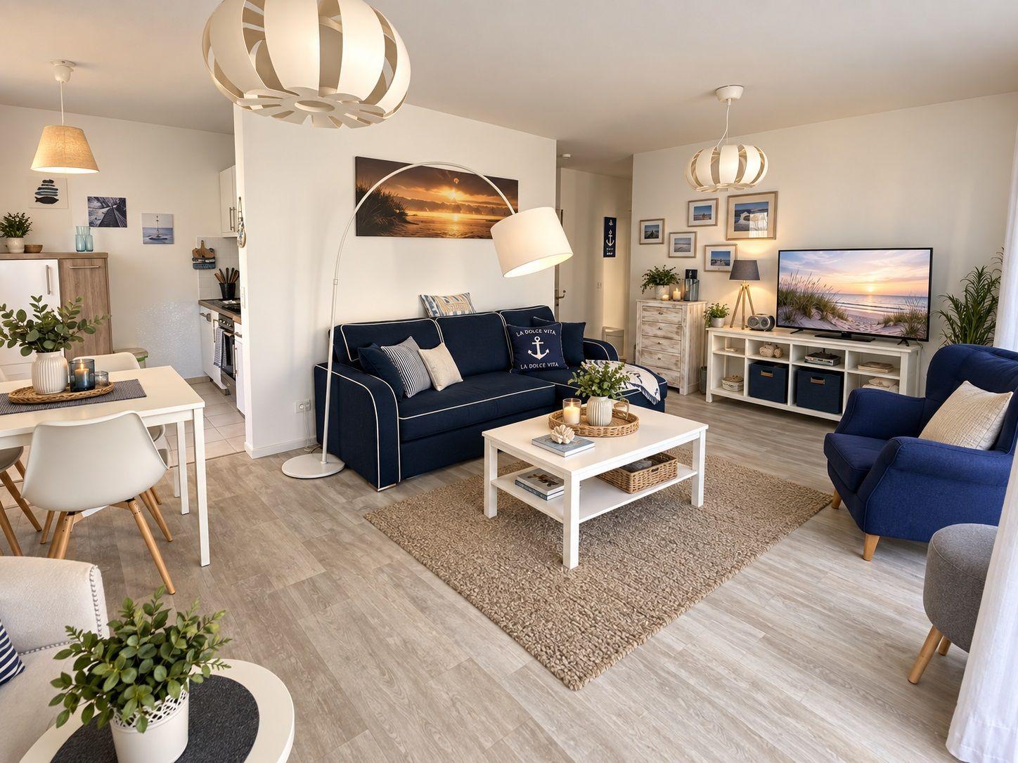 Wohnzimmer mit Sofa, Sessel und TV. Küche und Essbereich sichtbar.