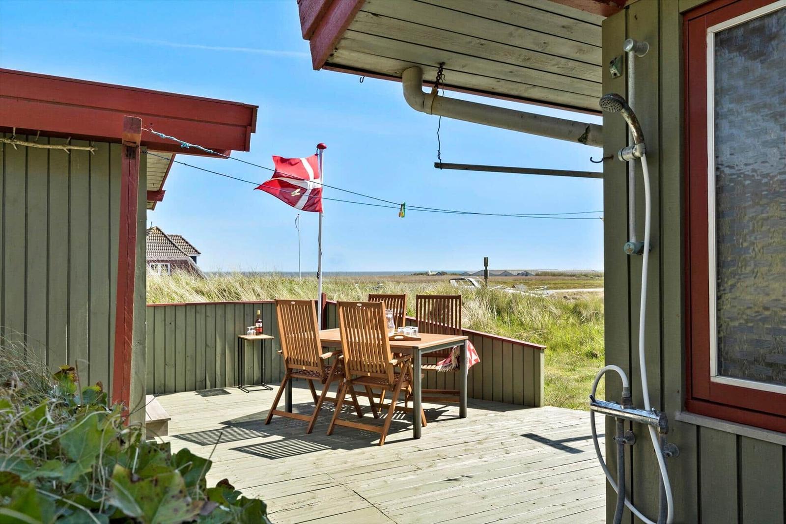 Weitläufiger Strand mit Dünen und Windkraftanlagen am Horizont.