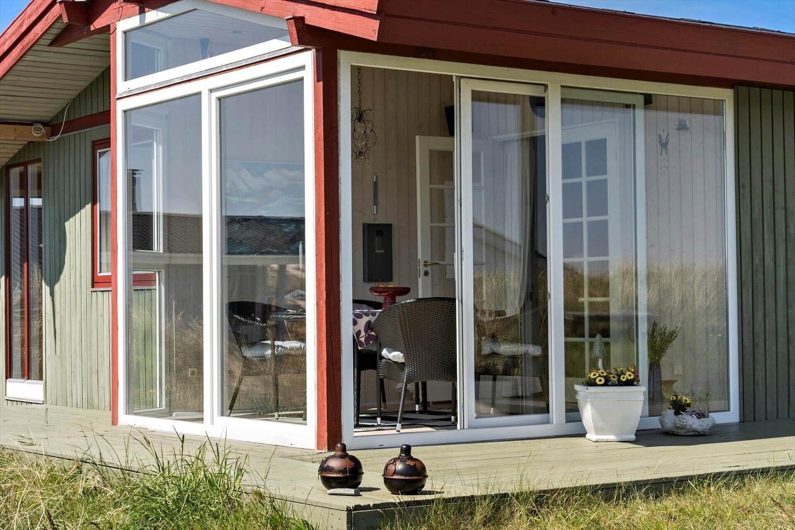 Modernes Ferienhaus mit Terrasse in Dünenlandschaft, Blick auf Meer und Windräder.