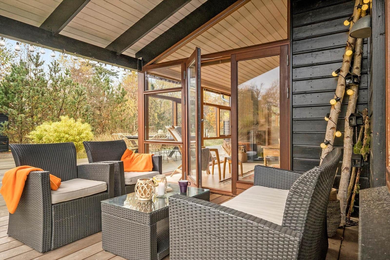 Terrasse mit Grill, Tisch, Stühlen und Sonnenschirm. Hintergrund: Wald und Gras.
