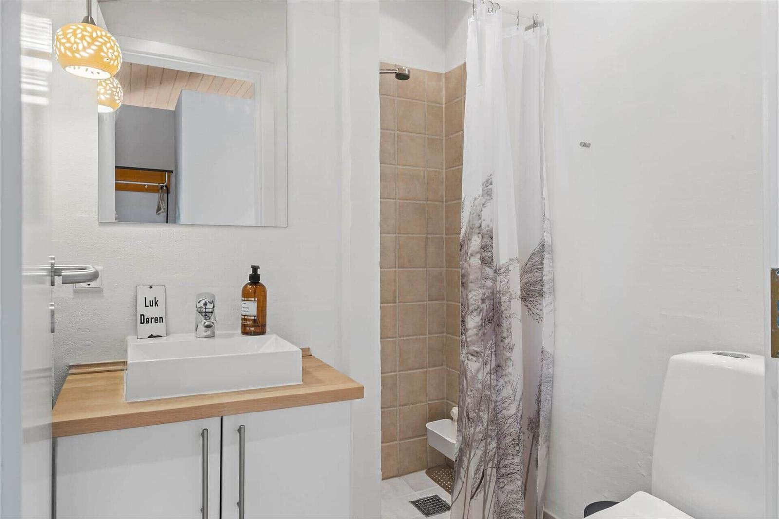 Zwei Betten mit grauen Bettdecken und bunten Kissen. Holzwände, weiße Kommode und Deckenlampe.