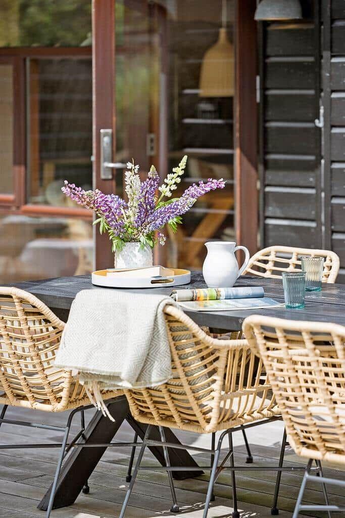 Terrasse mit Tisch, Stühlen und Sonnenschirm. Modernes Haus mit großem Fensterbereich.
