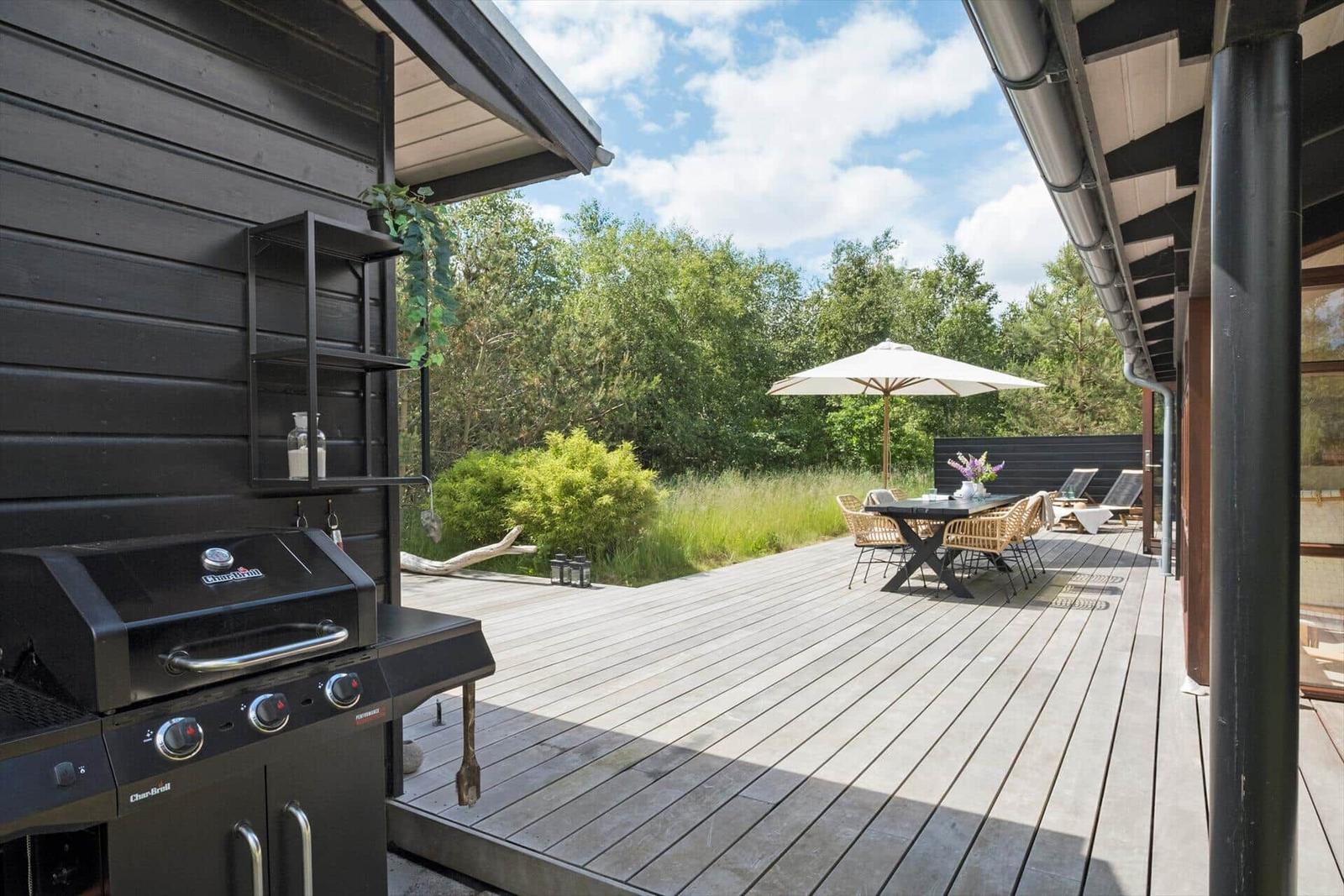 Terrasse mit Esstisch, Liegestühlen und Blumen. Holzdecke und Schutzdach.