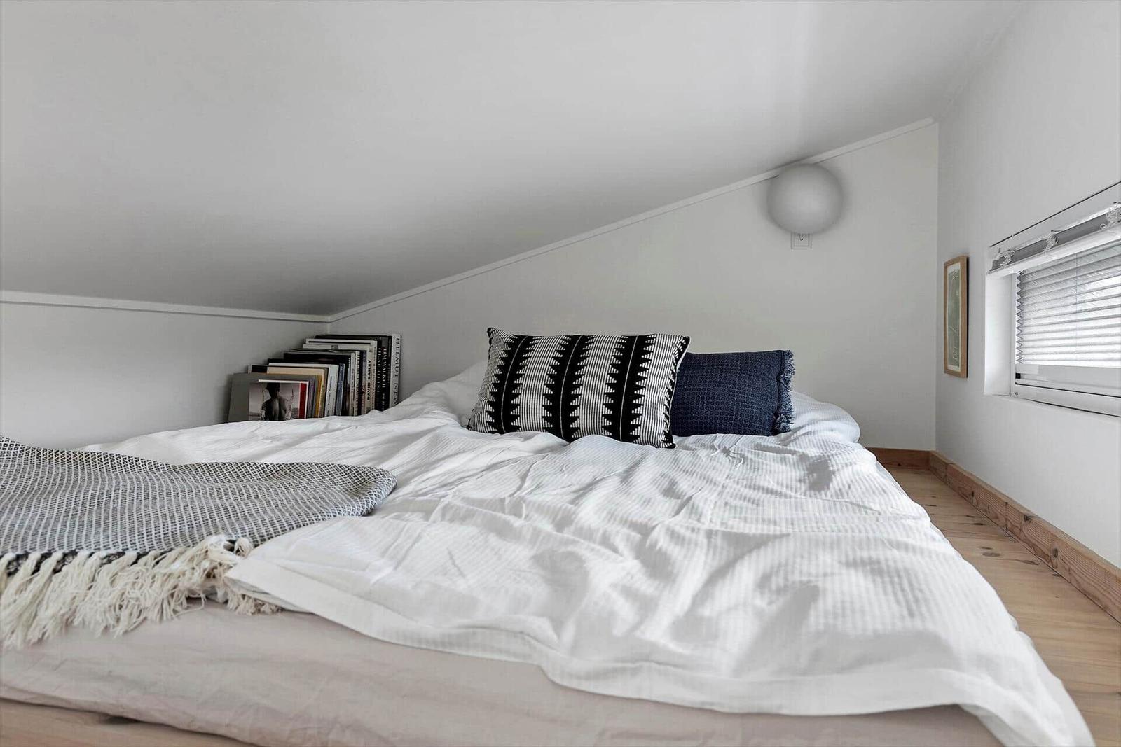Ein Schlafzimmer mit Bett, Fenster und Vorhängen. An der Wand hängt eine Lampe.