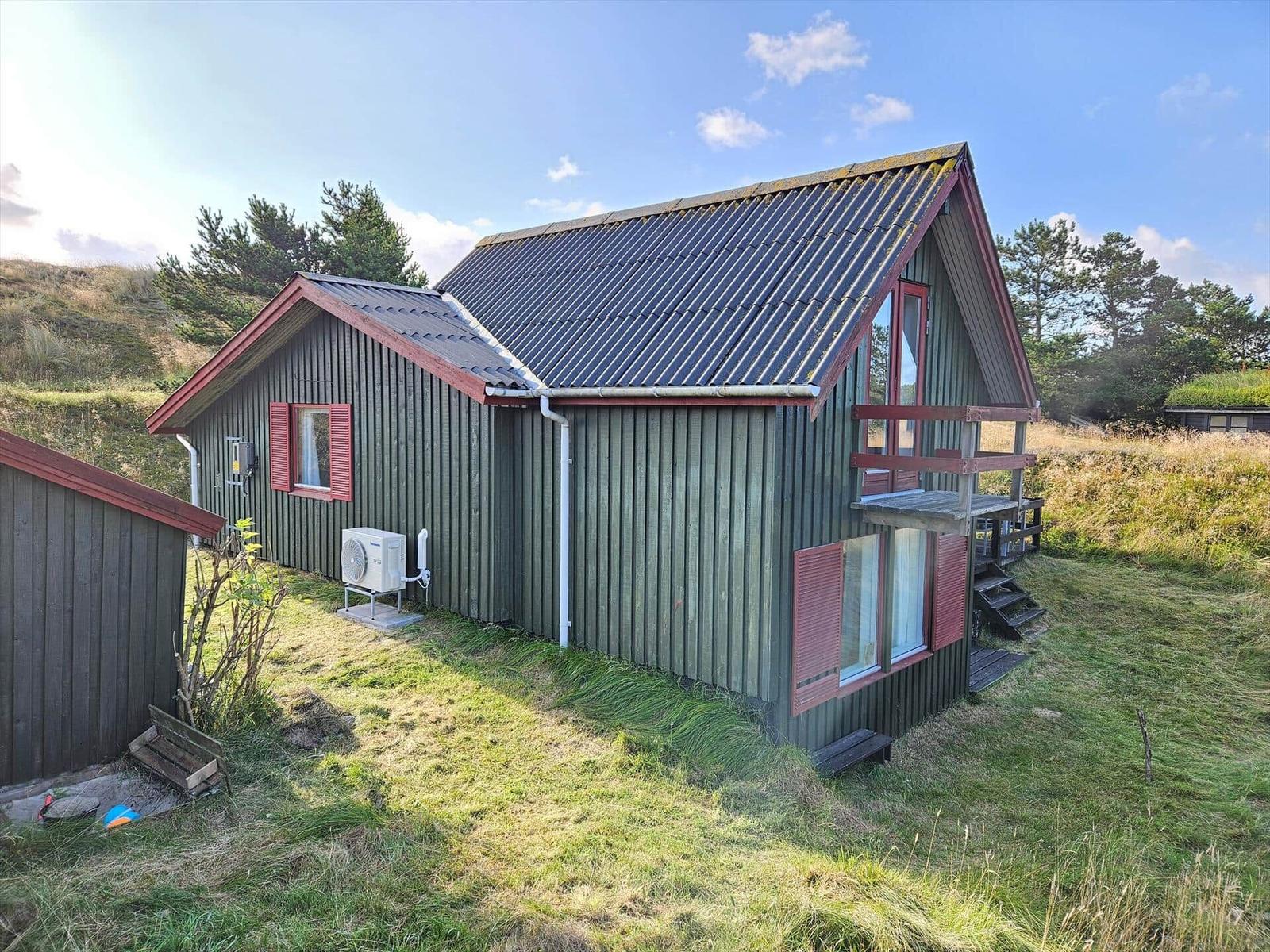 Grünes Holzhaus mit roter Tür, Picknicktisch und Gartenbereich.