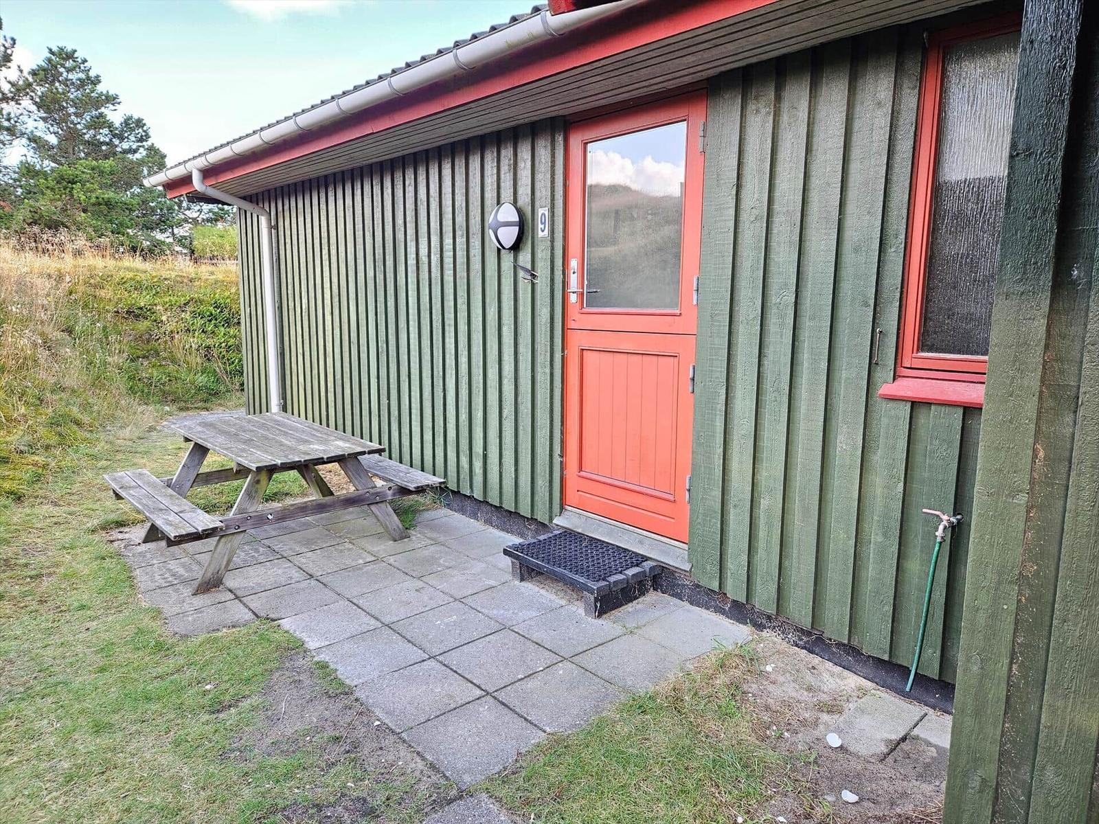 Holzhäuschen mit Terrasse und Grillplatz im Grasland.