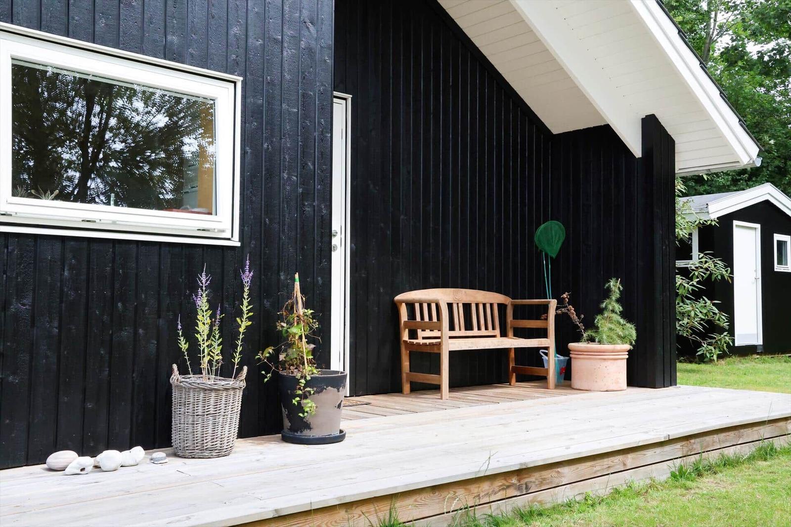 Wohnzimmer mit Fernseher, Holzwand und großem Fenster. Davor steht ein Holzregal mit Medien.