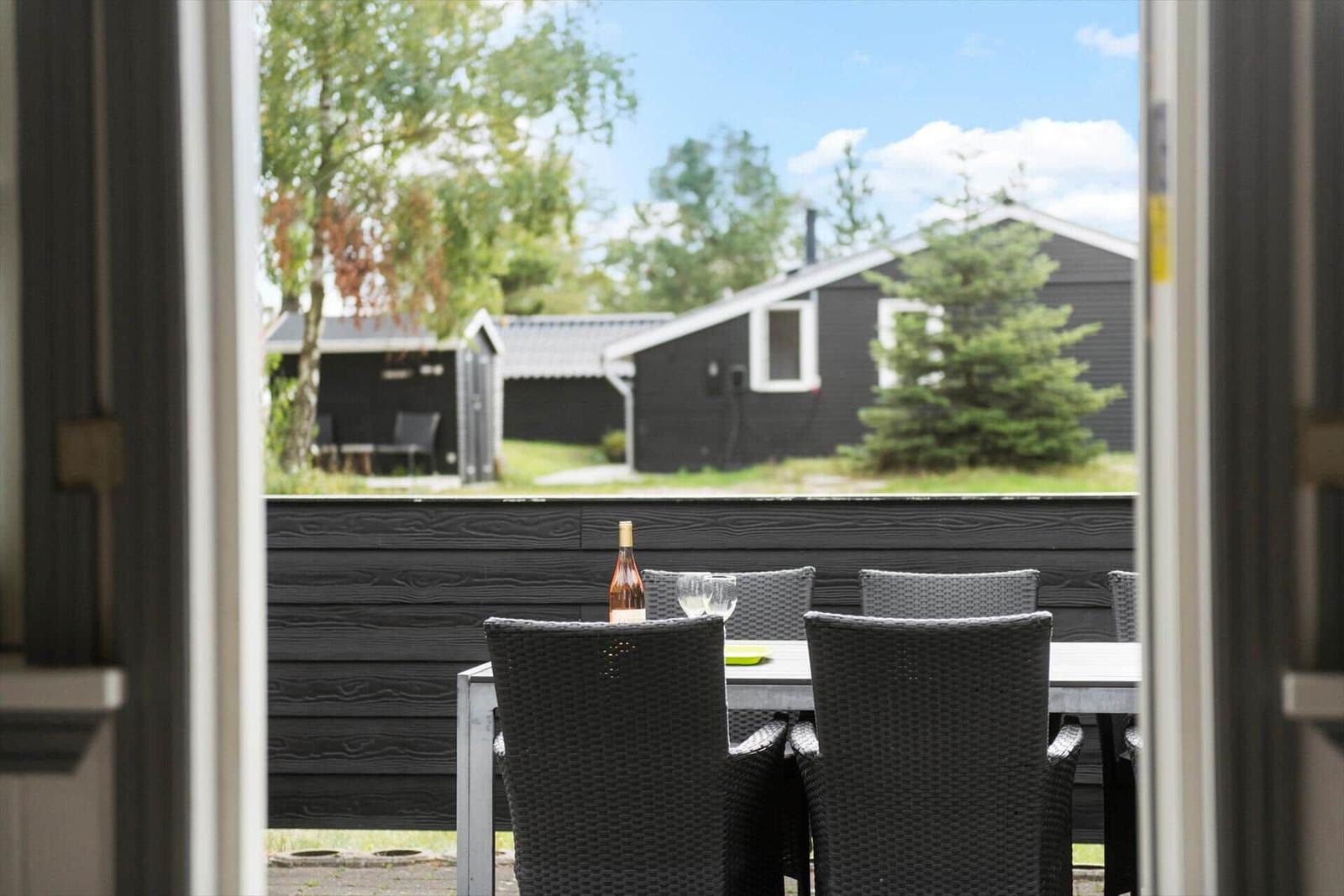 Black wooden cabin with terrace and garden. Adjacent shed. Surrounded by trees.