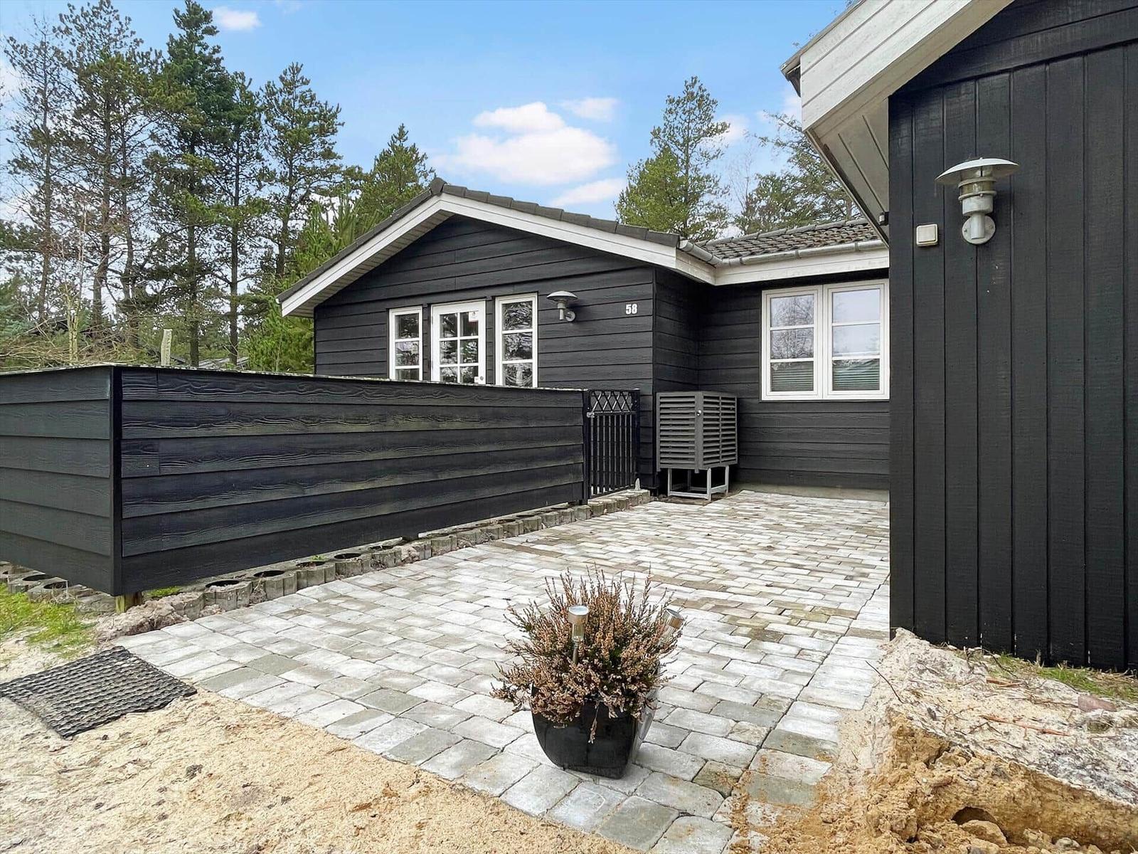 Black wooden cabin with white windows and terrace in the woods