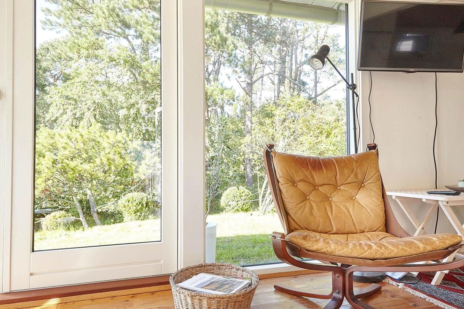 Weiße Gartenbank mit Tisch und Stühlen vor Holzstapel und Bäumen.