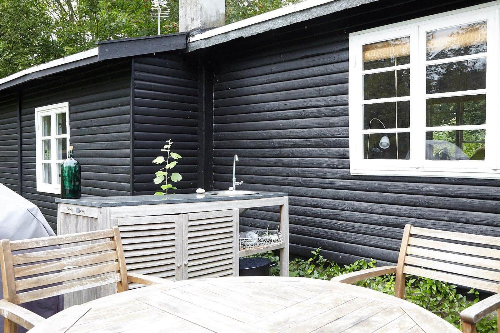 Holzterrasse mit Grill, Sitzbänken und Hängematte im Grünen.