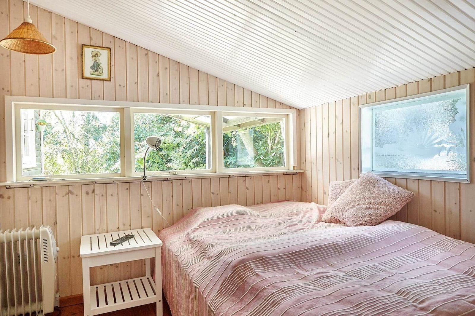 Ein dunkles Holzhaus mit weißem Fenster und Trampolin im grünen Garten.