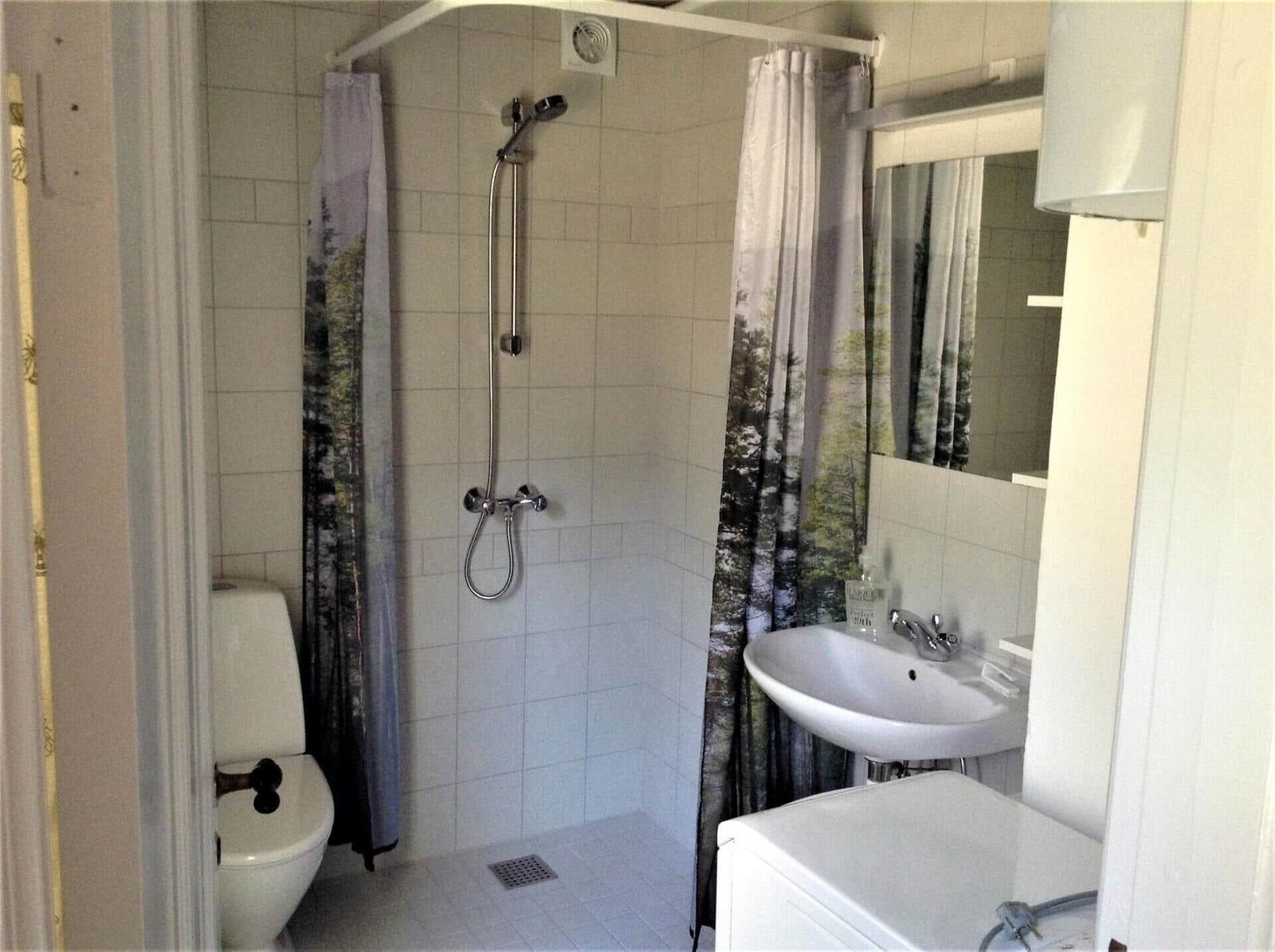 Durch ein rundes Fenster blickt man auf einen grasbewachsenen Hang mit Bäumen.