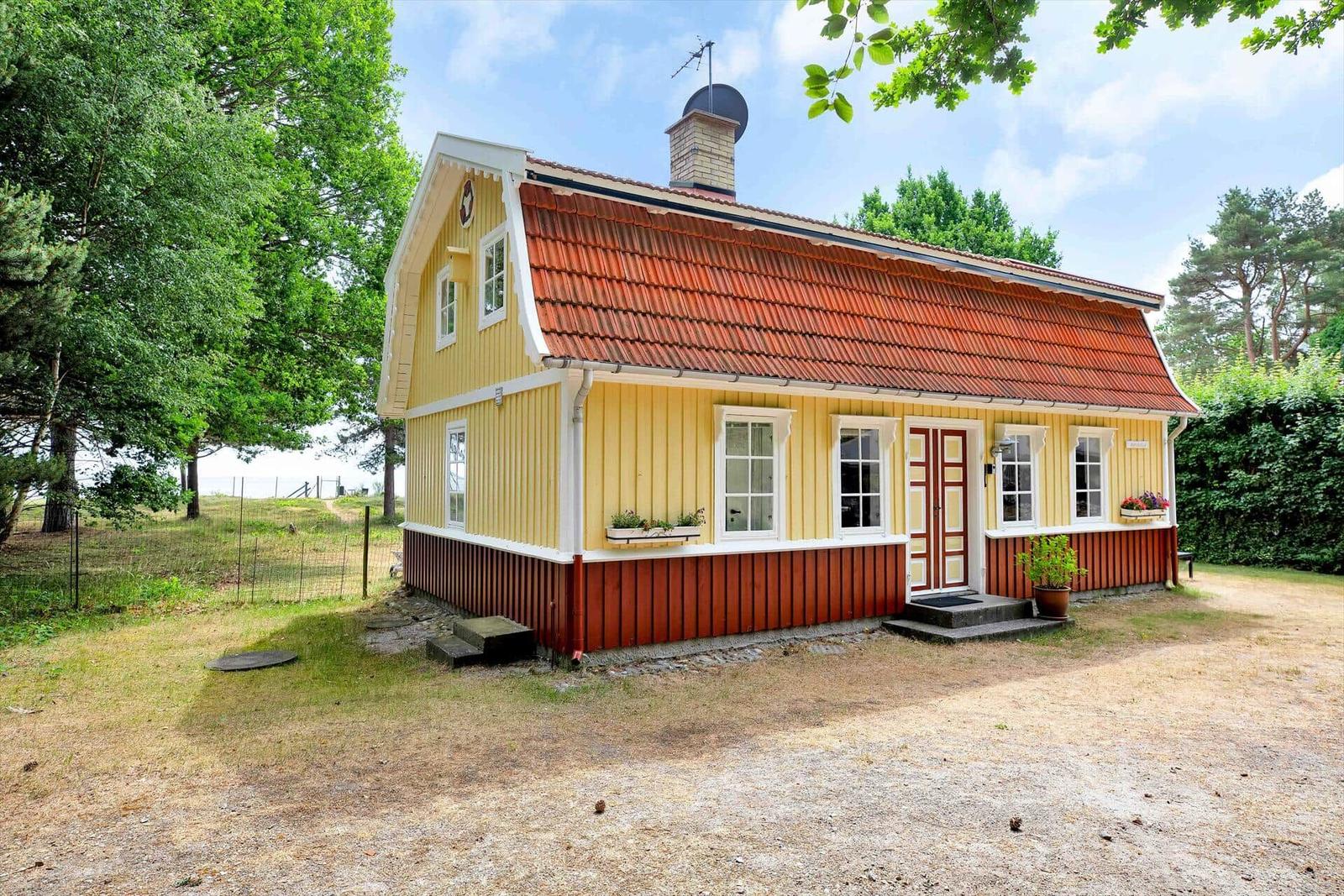 Ein Haus mit gelben Wänden und rotem Dach, umgeben von Wald und Gartenmöbeln.