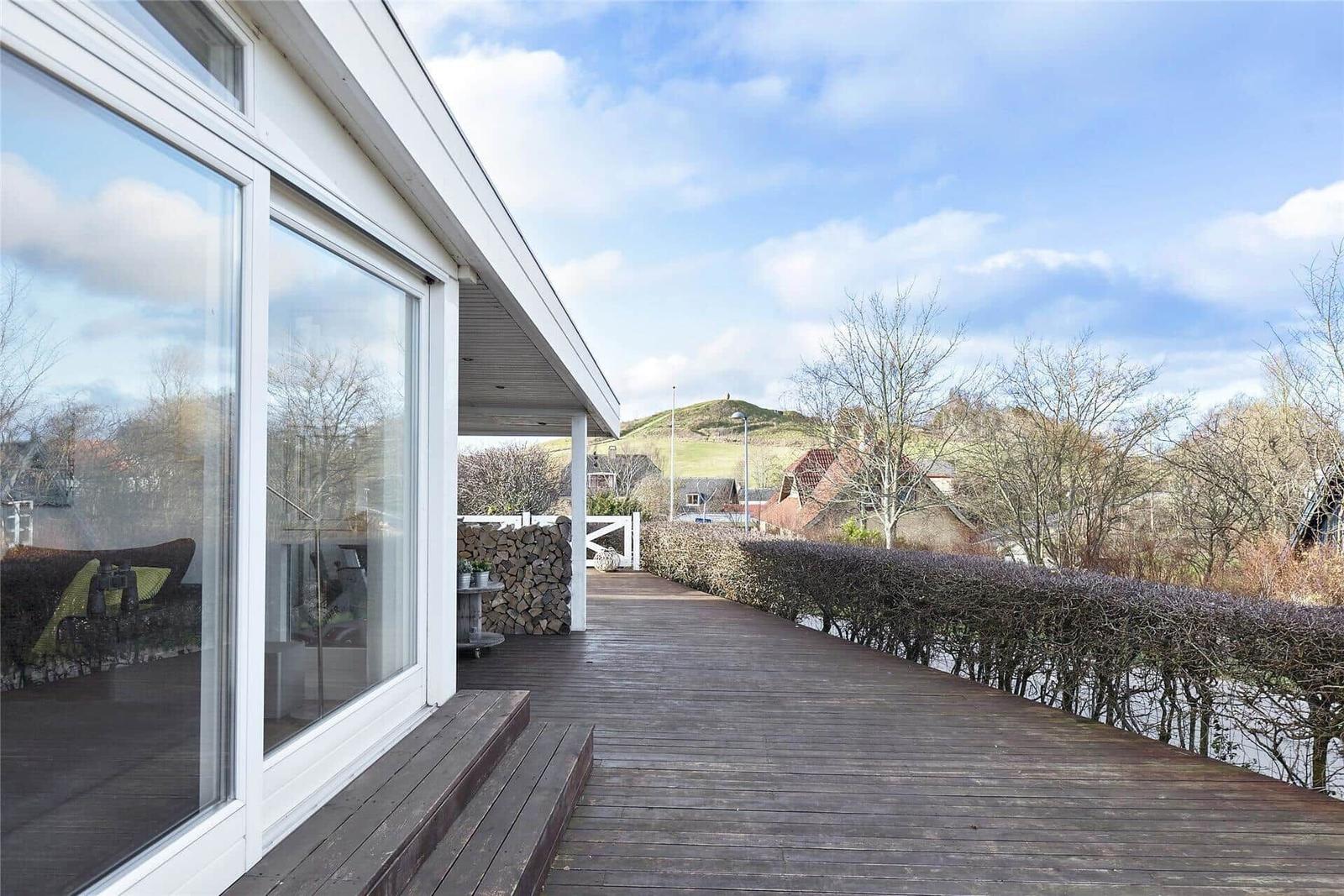 Haus mit Garten, Blumenhecke und Terrasse unter blauem Himmel.
