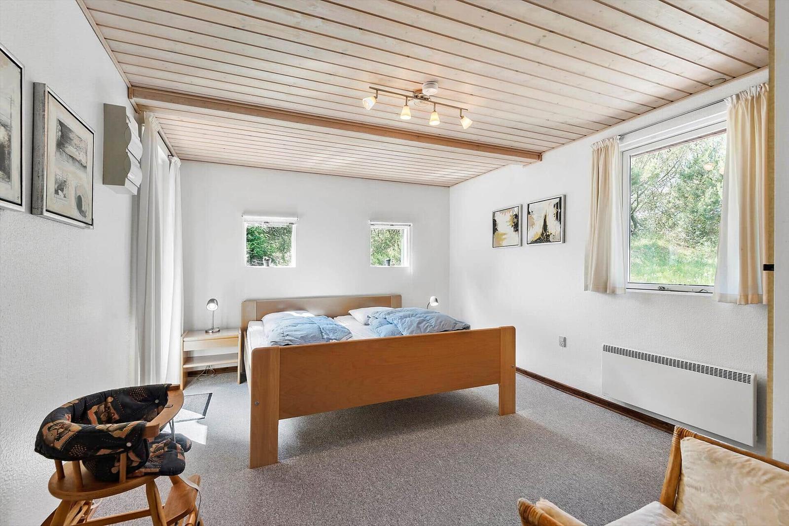 Schlafzimmer mit Bett, Nachttisch und Fenster mit Blick auf Bäume.